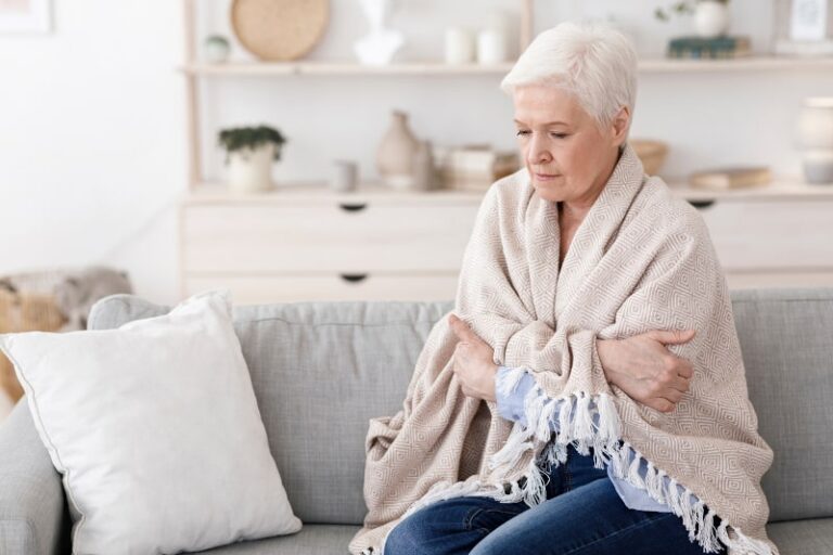 Cold elderly woman wrapped in blanket on couch